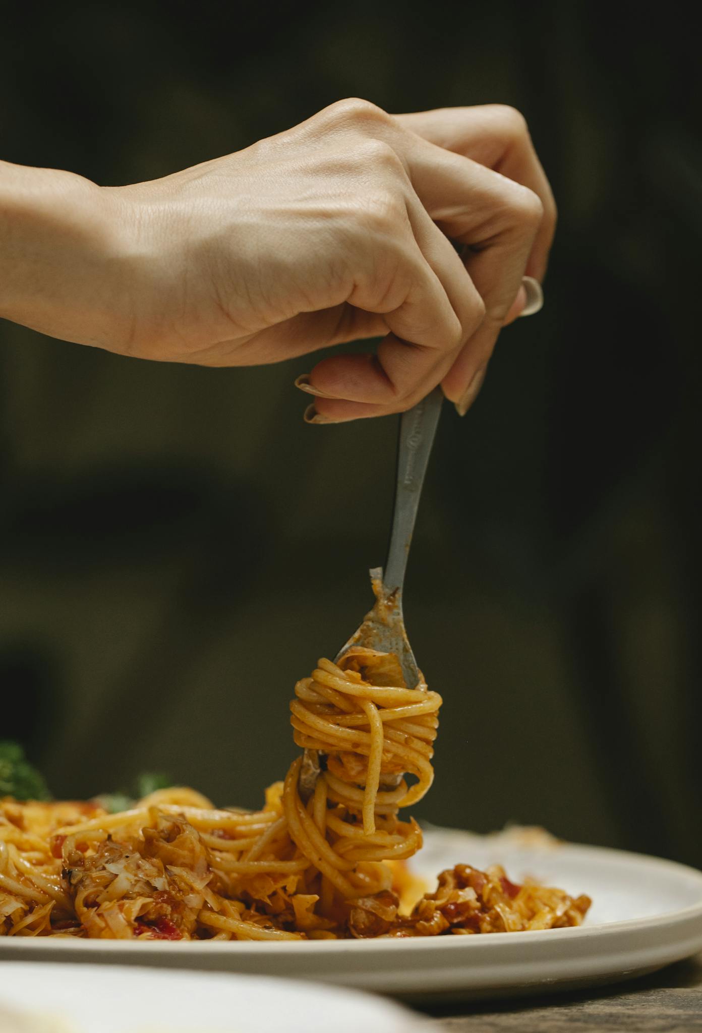 Crop faceless female using fork while eating yummy spaghetti alla bolognese during dinner in restaurant